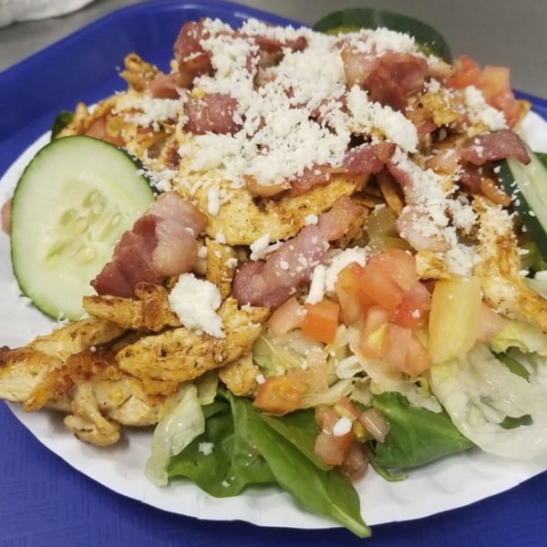 Mexican chicken salad with bacon, crumbled cheese, tomatoes, and cucumber slices on a white plate.
