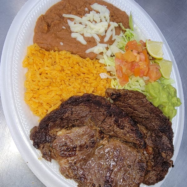 Mexican steak platter with rice, refried beans, guacamole, lettuce, tomato, and lime wedges.