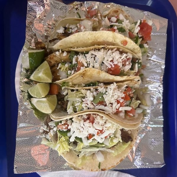 Four Armored Tacos with meat, lettuce, tomatoes, cheese, and lime wedges on foil.