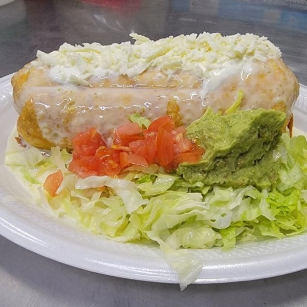 A large Mexican chimichanga topped with white sauce and cheese, served with shredded lettuce, diced tomatoes, and guacamole.