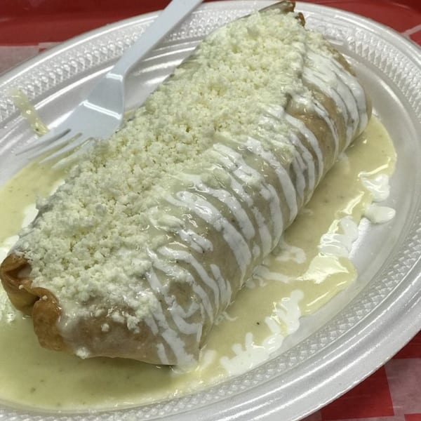 A large, cheese-covered burrito with white sauce on a white plate with a plastic fork.