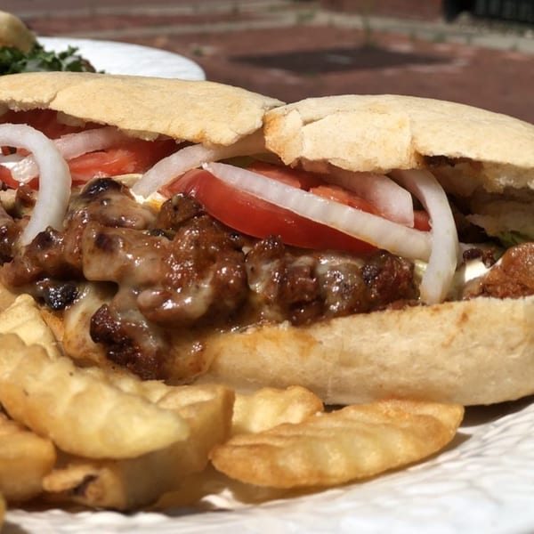 Two Mexican sandwiches filled with meat, melted cheese, tomatoes, and onions, served with fries.