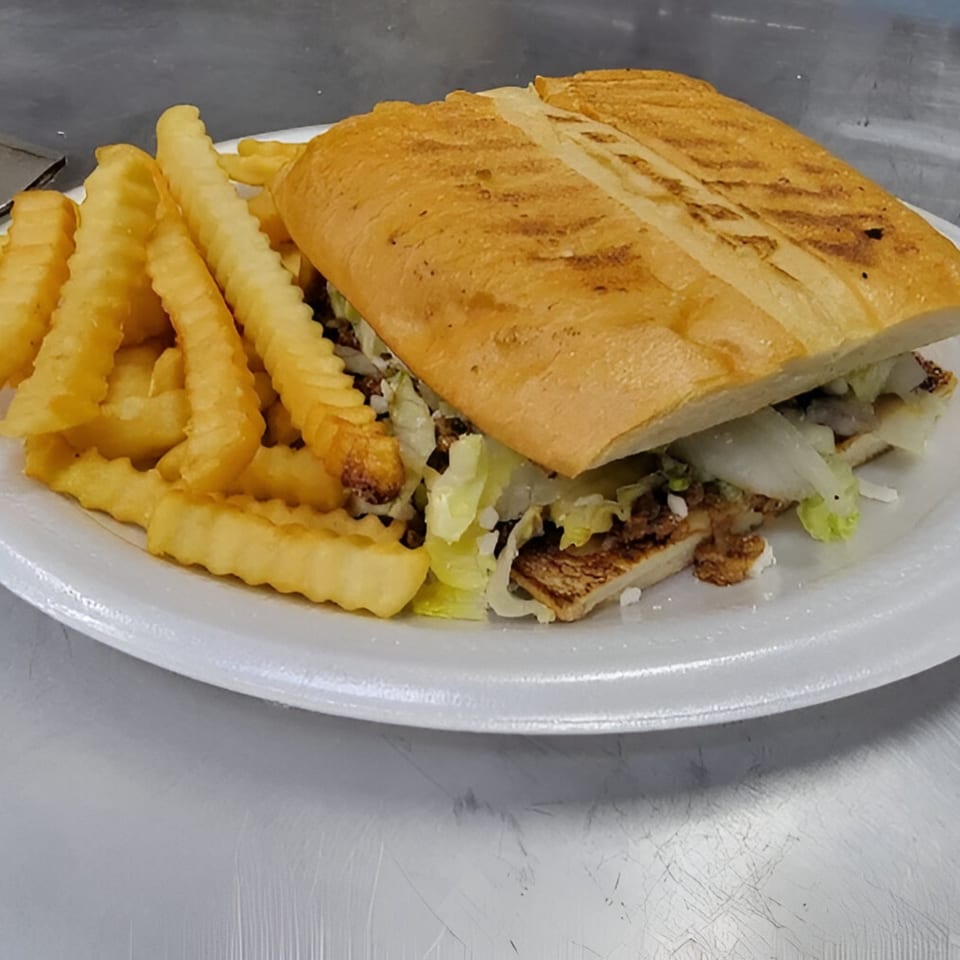 A Mexican torta sandwich with grilled bread, lettuce, and meat, served with crinkle-cut fries.
