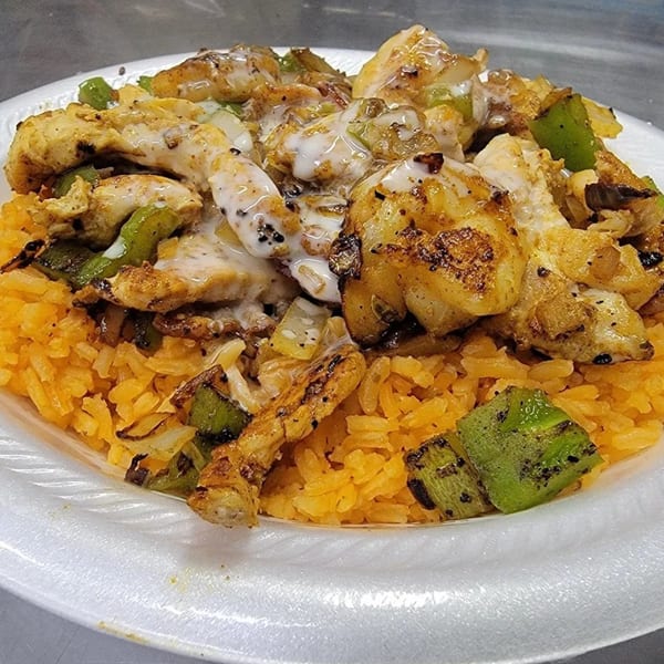 Grilled chicken and green peppers with white sauce over yellow rice on a white plate.