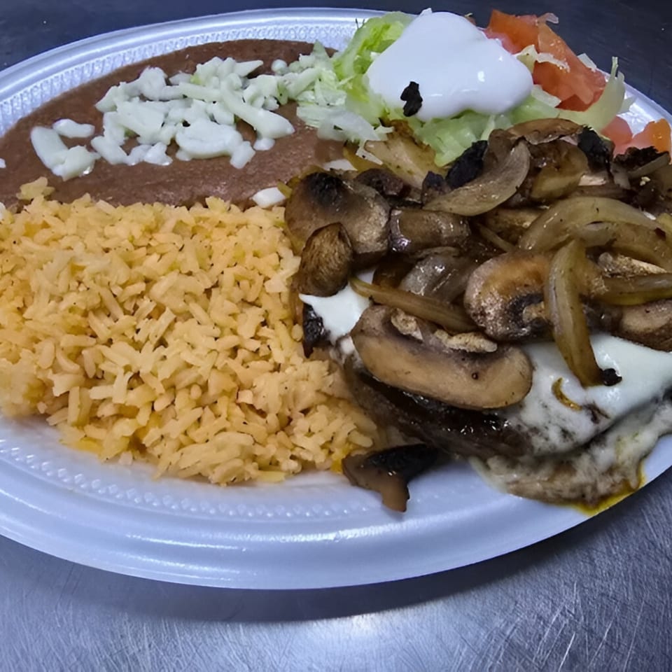 A Mexican dish with rice, refried beans, lettuce, tomato, sour cream, and grilled mushrooms and onions.