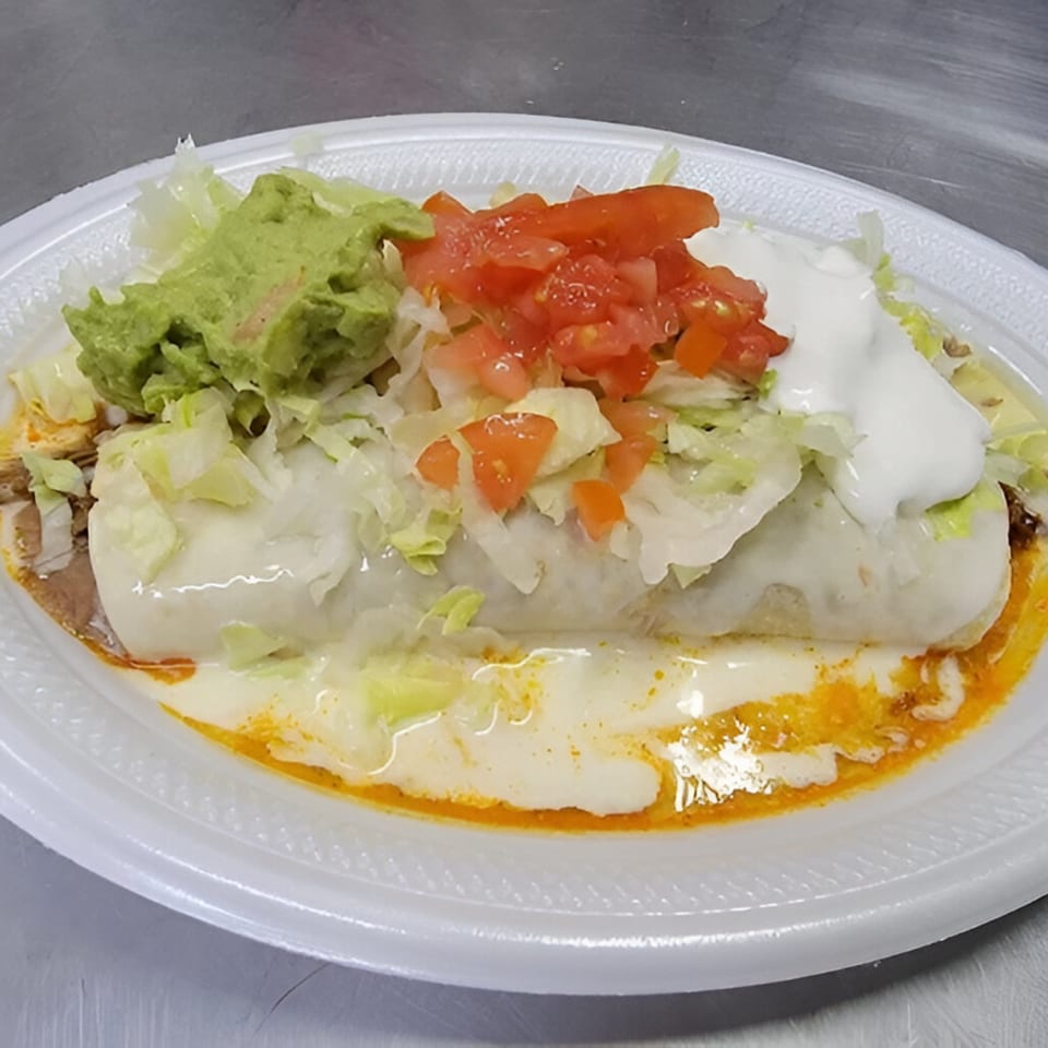 A large burrito covered in white sauce, topped with guacamole, diced tomatoes, and sour cream.